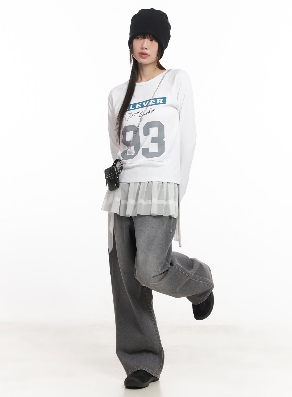 Venessa Washed Baggy Jeans CM528 in dark gray, dynamic full-body pose on model with leg raised, styled with graphic tee, sheer pleated layer, beanie, and chain bag.