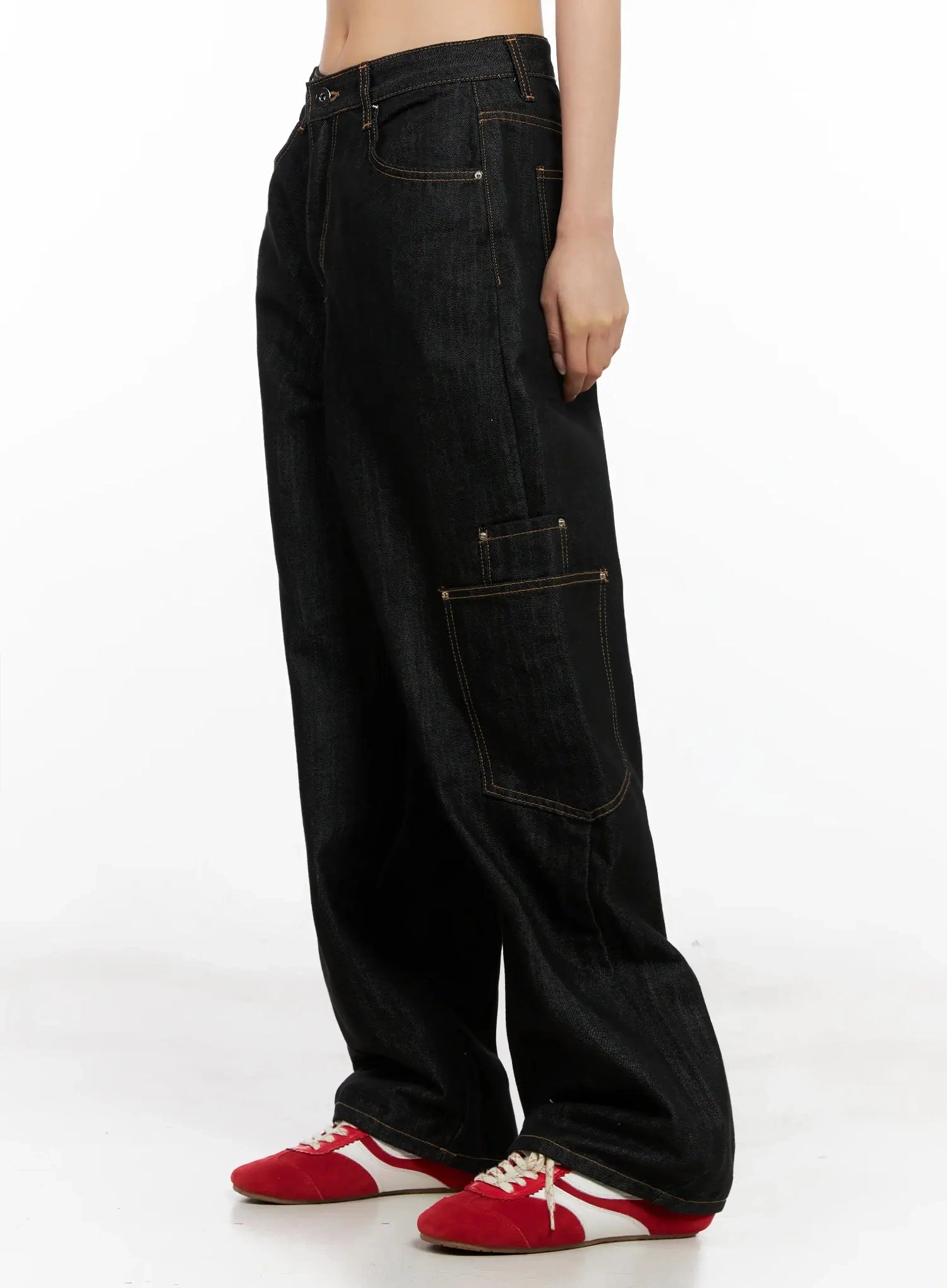 Dahee Wide-Leg Cargo Jeans IG508 in black, pure side view on headless model, side cargo pocket with rivet detail and contrast stitching clearly visible, relaxed wide-leg fall, styled with red sneakers.