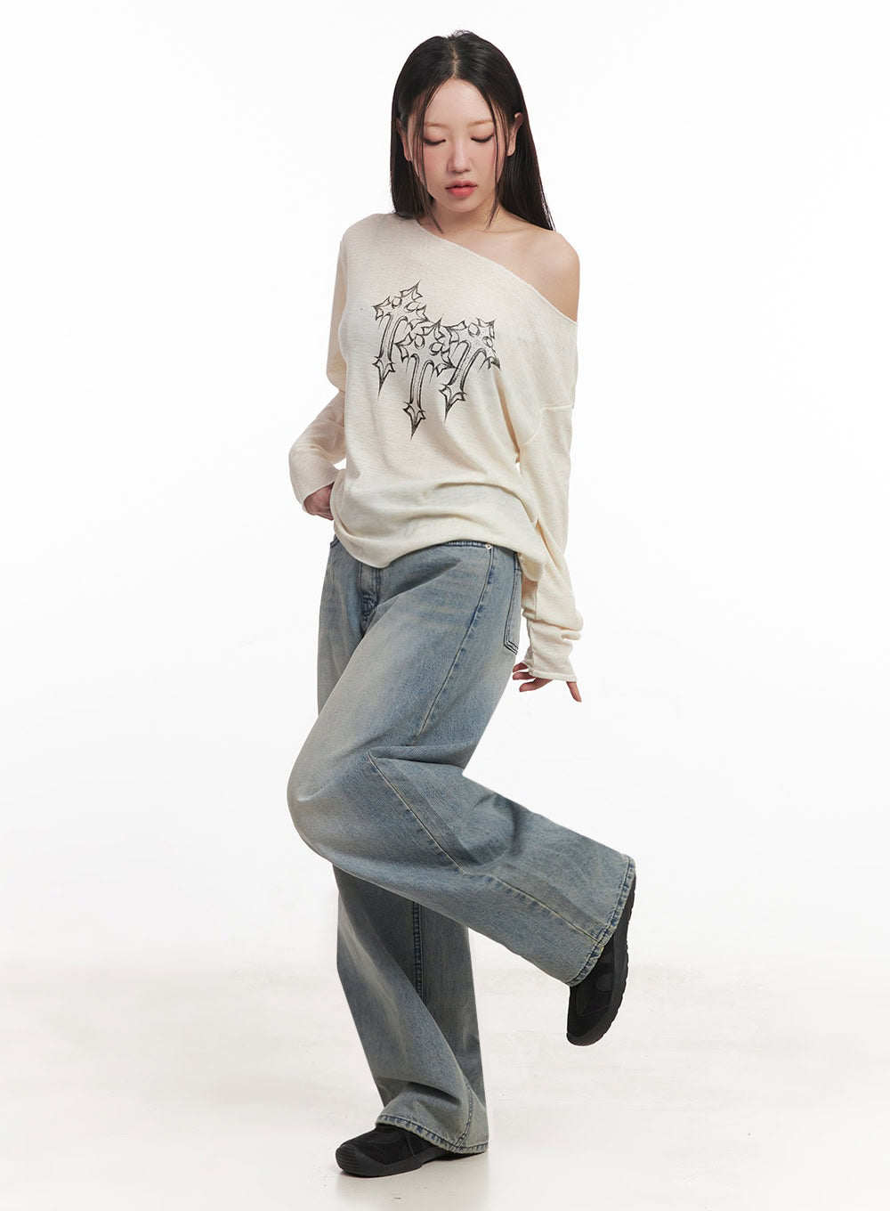 Casey Washed Baggy Jeans IM528 in light blue, dynamic side-angled full shot on model mid-step, wide-fit washed denim with contrast stitching visible, styled with cream off-shoulder knit and black shoes.