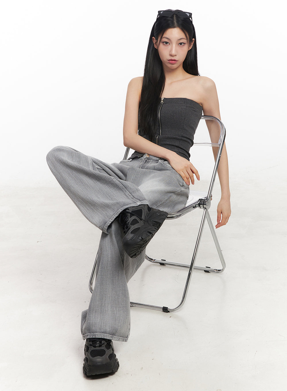 Flore Washed Wide-Leg Jeans IY516 in gray, full-body seated editorial shot on model, wide-leg denim drapes over chunky sneakers, styled with dark zip tube top on chrome folding chair.