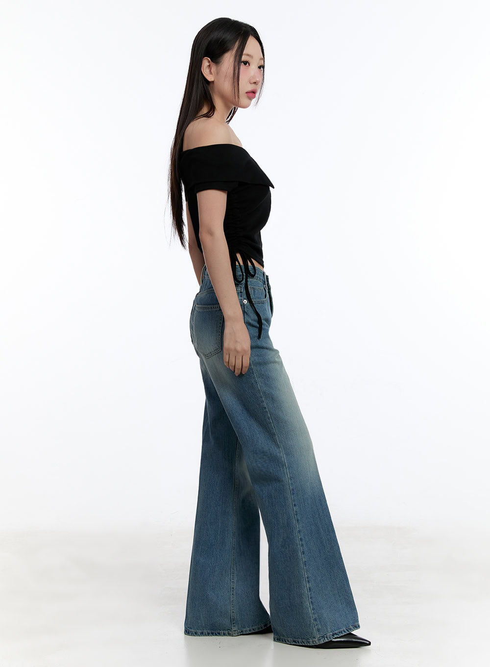 Aliya Washed Bootcut Jeans IU503 in dark blue, side-view full-body shot on model, wide-fit washed denim showing bootcut silhouette and back pocket placement, paired with black crop top.