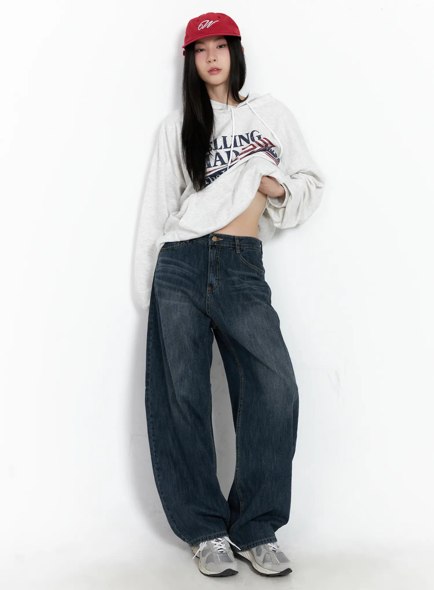 Seoy Washed Denim Jeans CG525 in dark blue, full-length front shot on model posed against wall, hoodie lifted to show waistband and front pockets, red cap styling.