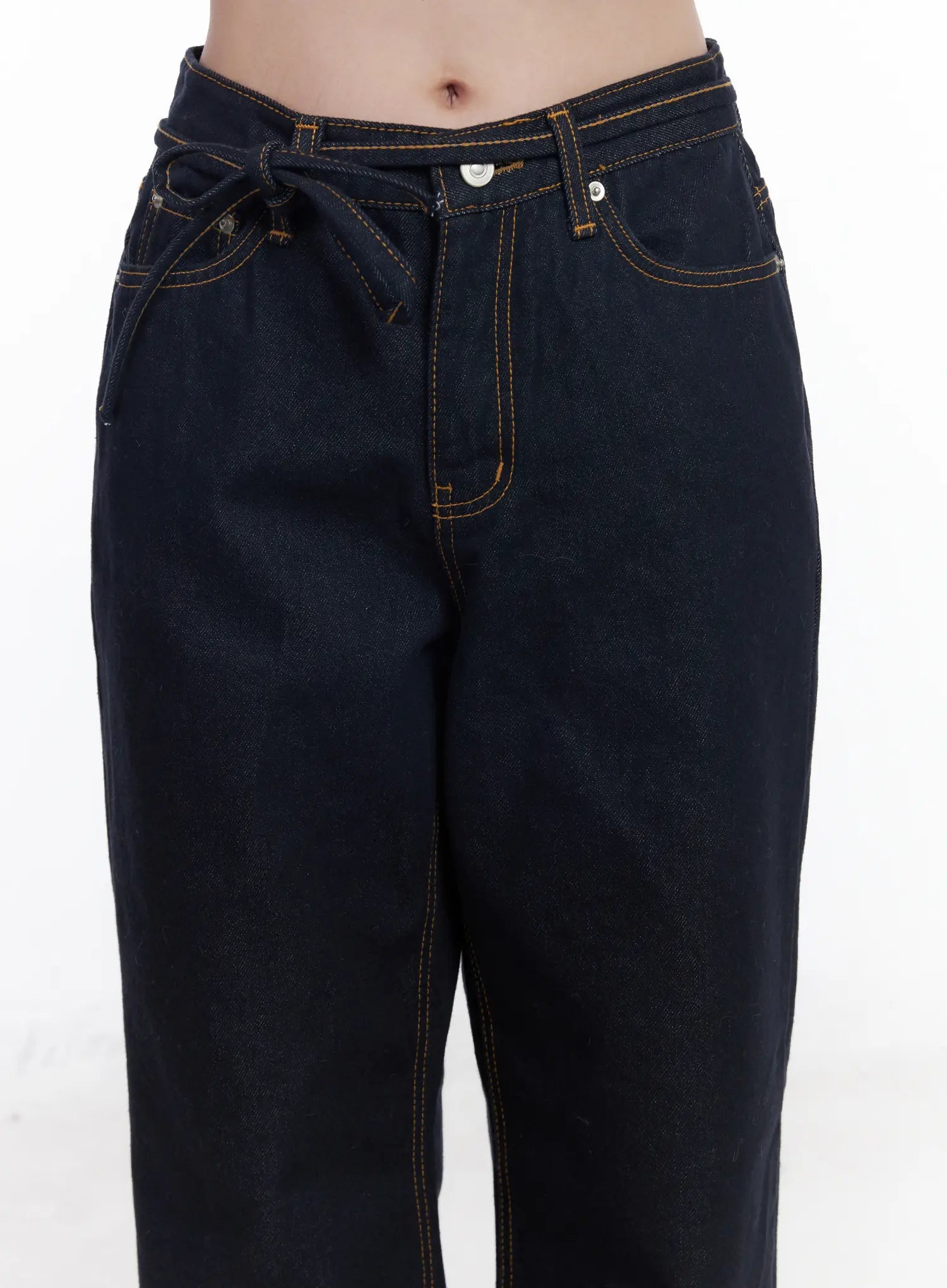 Mingi Non-Fade Semi-Wide Belted Jeans CJ519 in dark blue, waist close-up on model, knotted self-belt detail, contrast orange topstitching, front pockets and button fly visible.