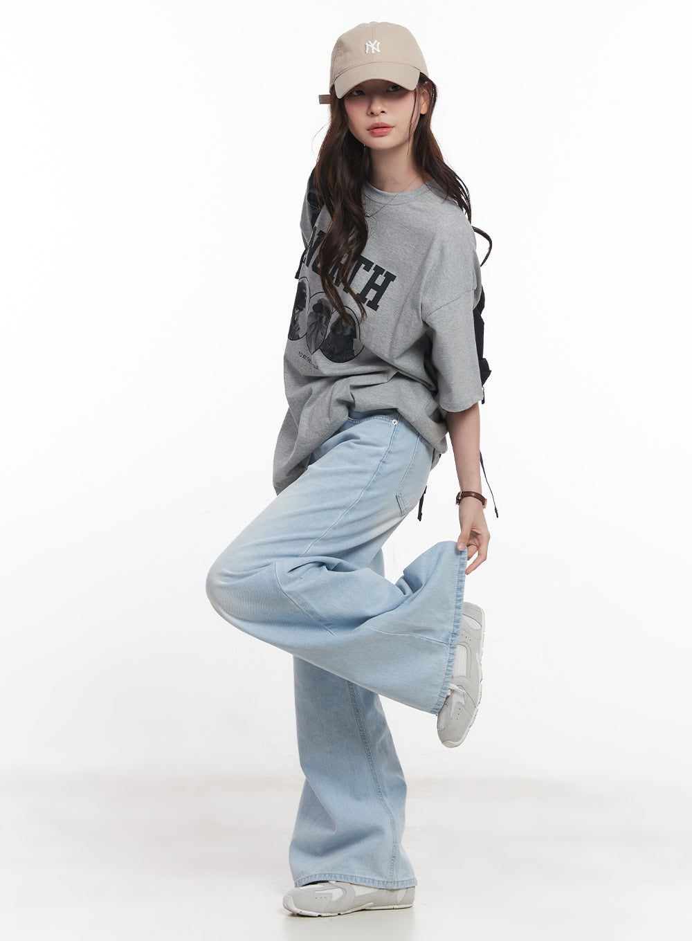 Judie Washed Wide-Leg Jeans CY519 in light blue, dynamic side-angle full-body shot on model lifting leg, showing voluminous wide-leg washed denim hem, styled with cap and gray tee.