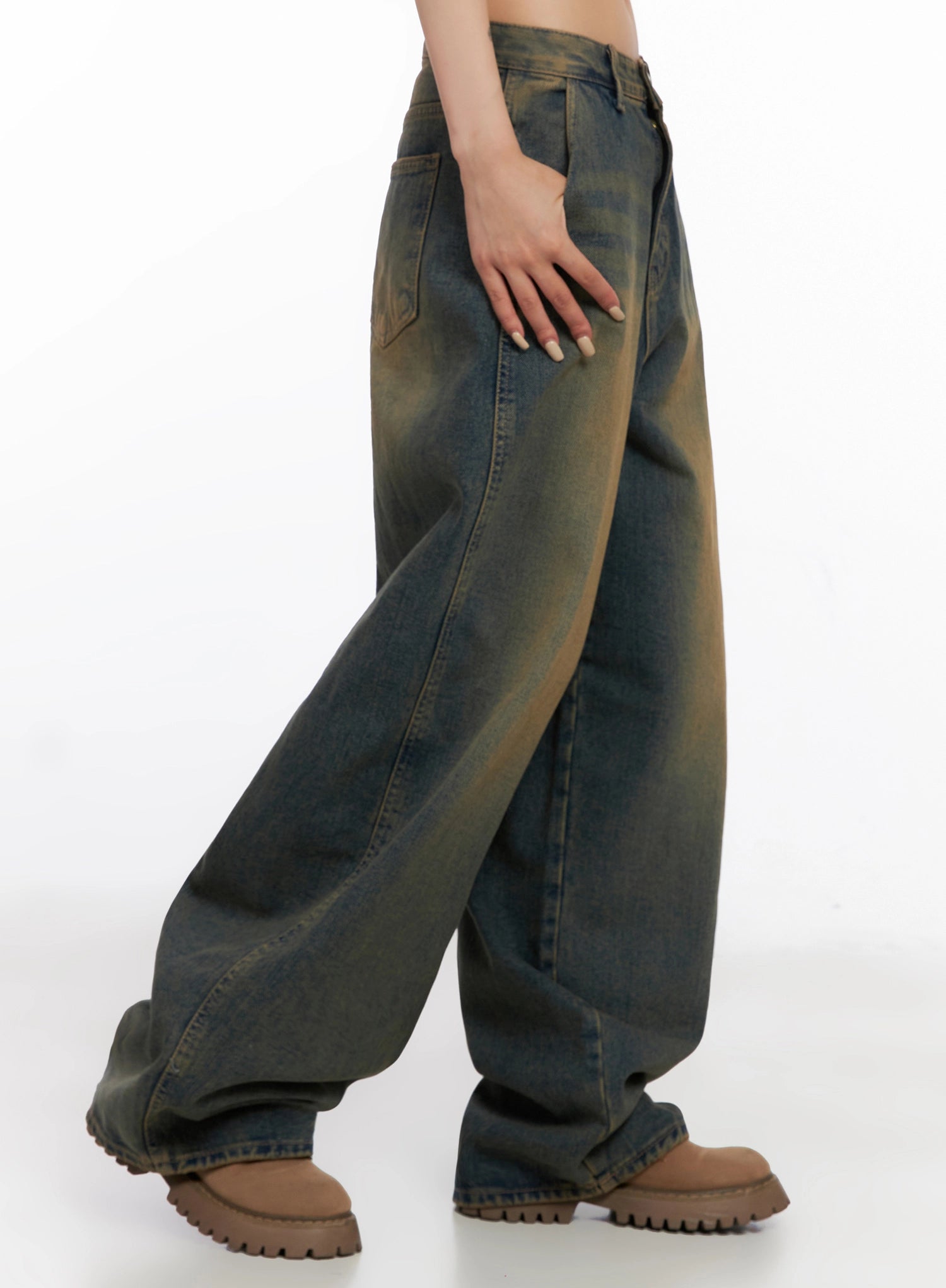 Minju Vintage Washed Baggy Jeans IS508 in dark blue, side waist-to-hem shot on model with hand on hip, showing pocket placement and heavy faded yellow-blue cotton wash drape, brown boots.