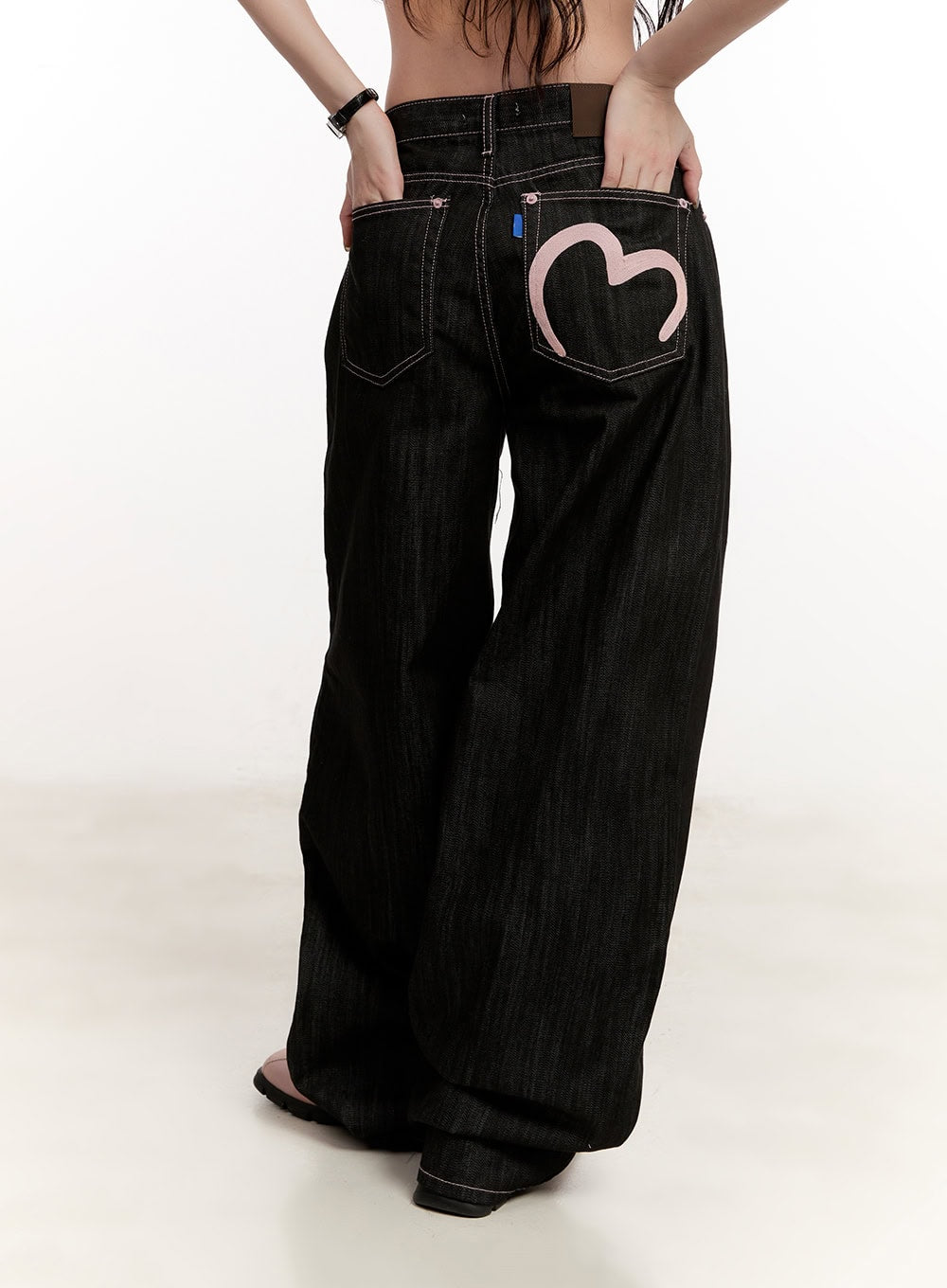 Trinity Stitched Baggy Jeans CM510 in black, back three-quarter view on model, pink heart pocket embroidery and contrast stitching clearly visible, ultra-wide baggy leg silhouette.