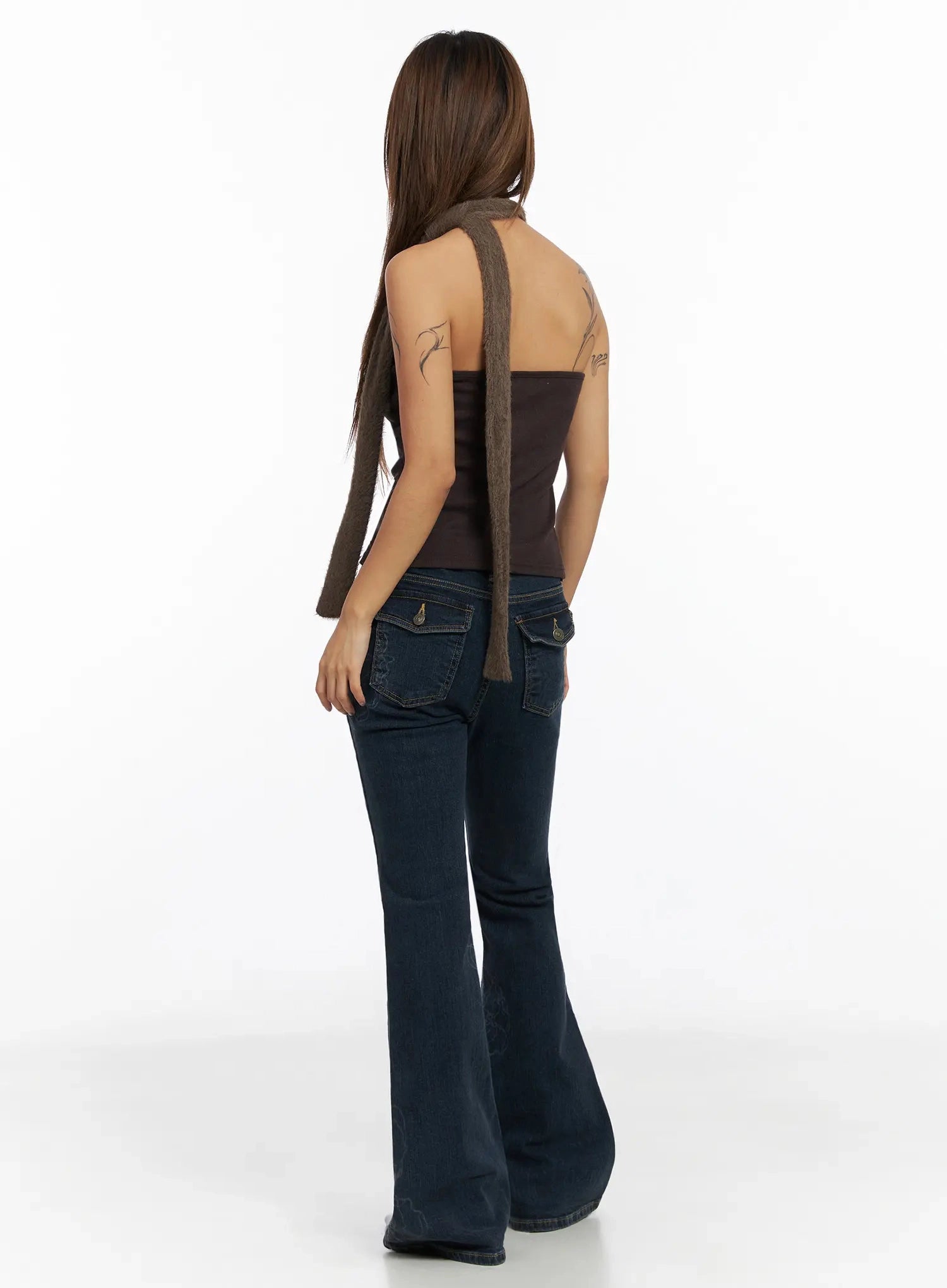 Amari Floral Embriodered Bootcut Jeans IN528 in dark blue, back full-length shot on model, showing flap back pockets with gold hardware and wide bootcut flare, paired with brown halter top and scarf.