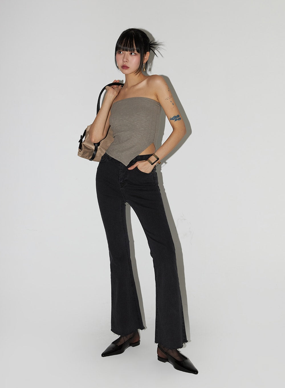 Mid Waist Button Flared Jeans IF402 in dark grey, 3/4 front editorial shot on model holding bag, mid-rise waist with pocket detail, flared raw-hem leg, styled with mocha tube top and black flats.