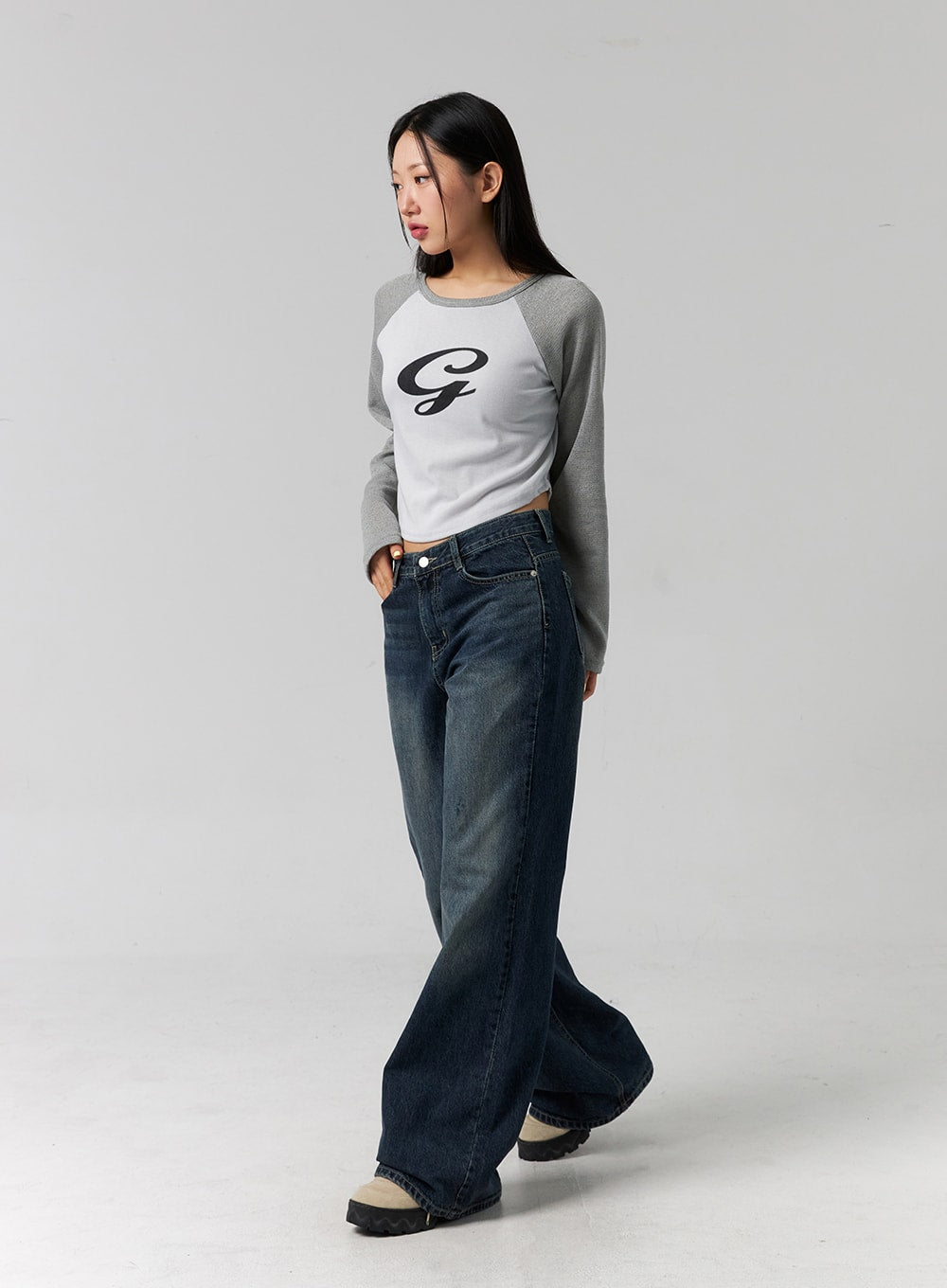 Low Rise Washed Wide Jeans CG315 in dark blue, three-quarter side-angle on model looking aside, low-rise wide-leg washed denim, full-length drape to floor, styled with grey raglan crop top.