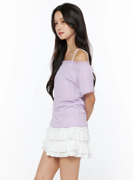 Lace Trim Off-Shoulder Tee CU522 in light purple, side profile on model, lace trim at neckline and sleeve cuff, slightly fitted waist, paired with white ruffle mini skirt, hands behind back.