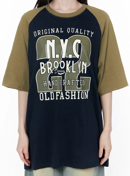 Casual Loose Fit Graphic Tee CU519 in dark blue, front graphic close-up on model torso, detailed NYC Brooklyn Old Fashion varsity-style print in olive and cream on navy cotton body, raglan seam visible.