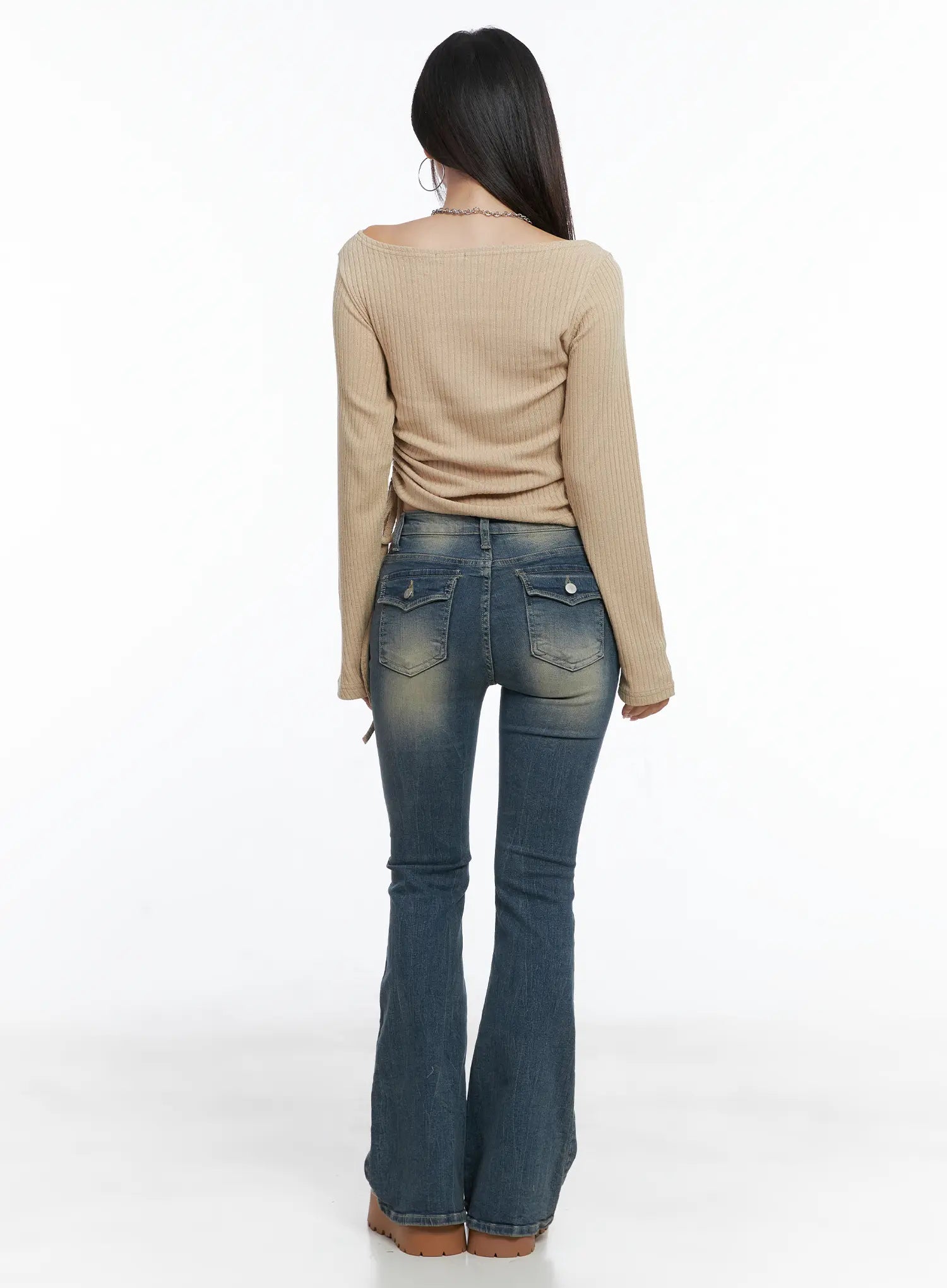 Sloan Vintage Hip Pad Flare Jeans CS502 in dark blue, full-length back outfit shot, model in beige ribbed top, flap pockets and flare hem fully visible, acubi casual styling.