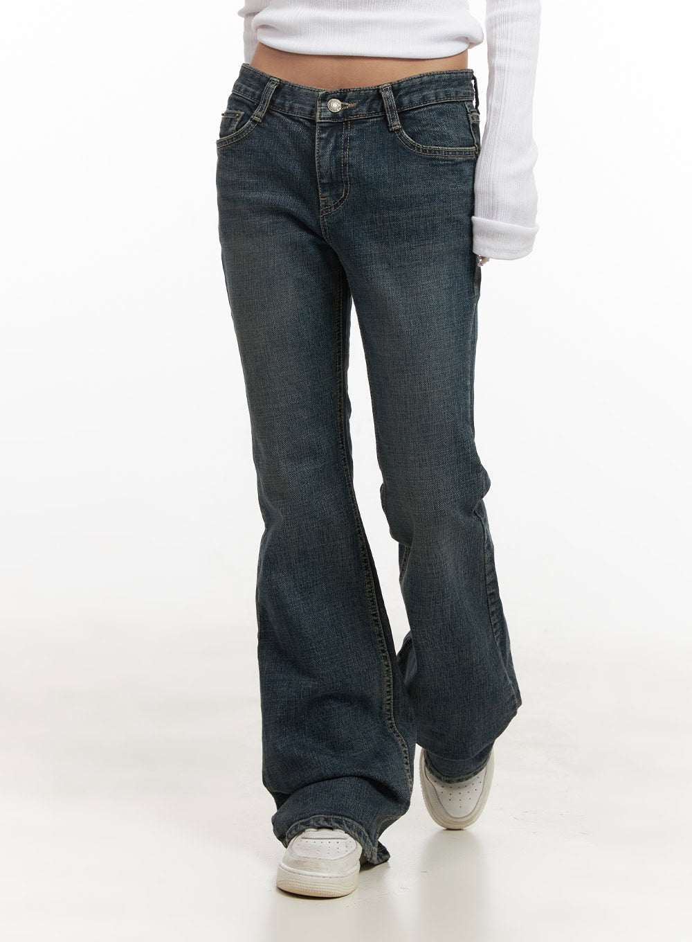 Natalia Low-Rise Flared Jeans CJ508 in dark blue, front mid-shot on model in motion, low-rise waist with button closure, washed slim denim flaring at ankle, paired with white ribbed long-sleeve top and sneakers.