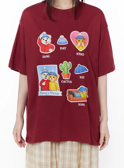Oversized Graphic Print Tee CU519 in dark red, front graphic close-up on model, detailed view of colorful Dang & Nyao cartoon sticker prints including DANG, HAT, NYAO, CACTUS, and SOFA motifs.