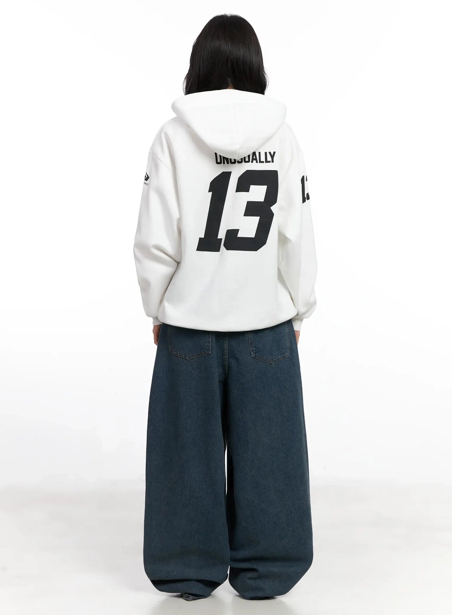 Aleena Mid-Wash Baggy Jeans IN528 in dark blue, back full-length shot on model in white graphic hoodie, revealing back patch pockets with silver button detail and balloon leg width.