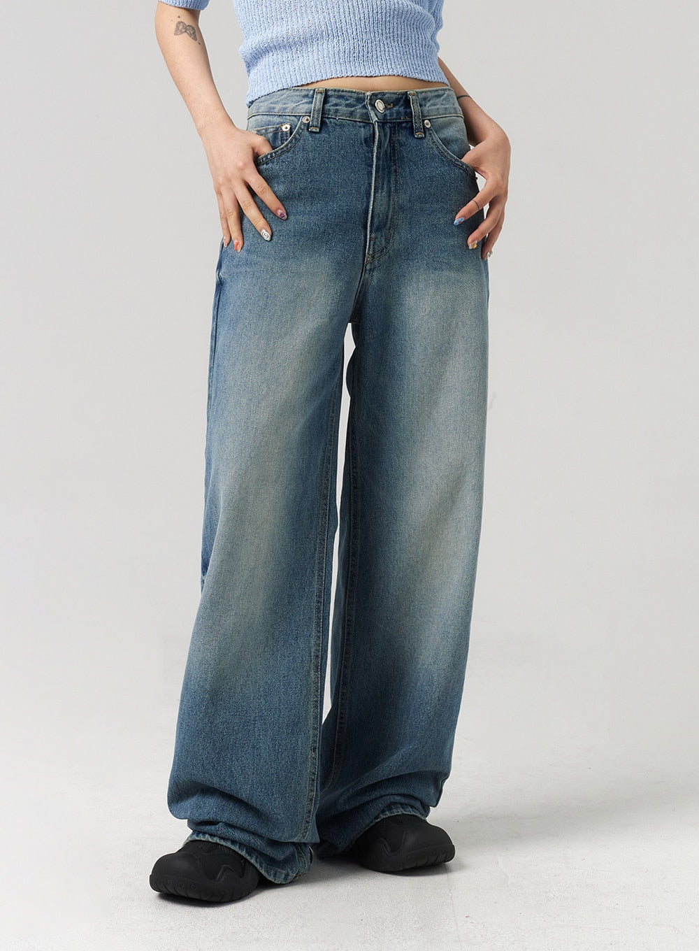 Mid-Wash Baggy Jeans CL312 in mid-wash blue, front waist-to-hem close-up on model, low-rise waistband with rivet hardware, wide-leg silhouette with sun-faded wash and hem bunching at floor.