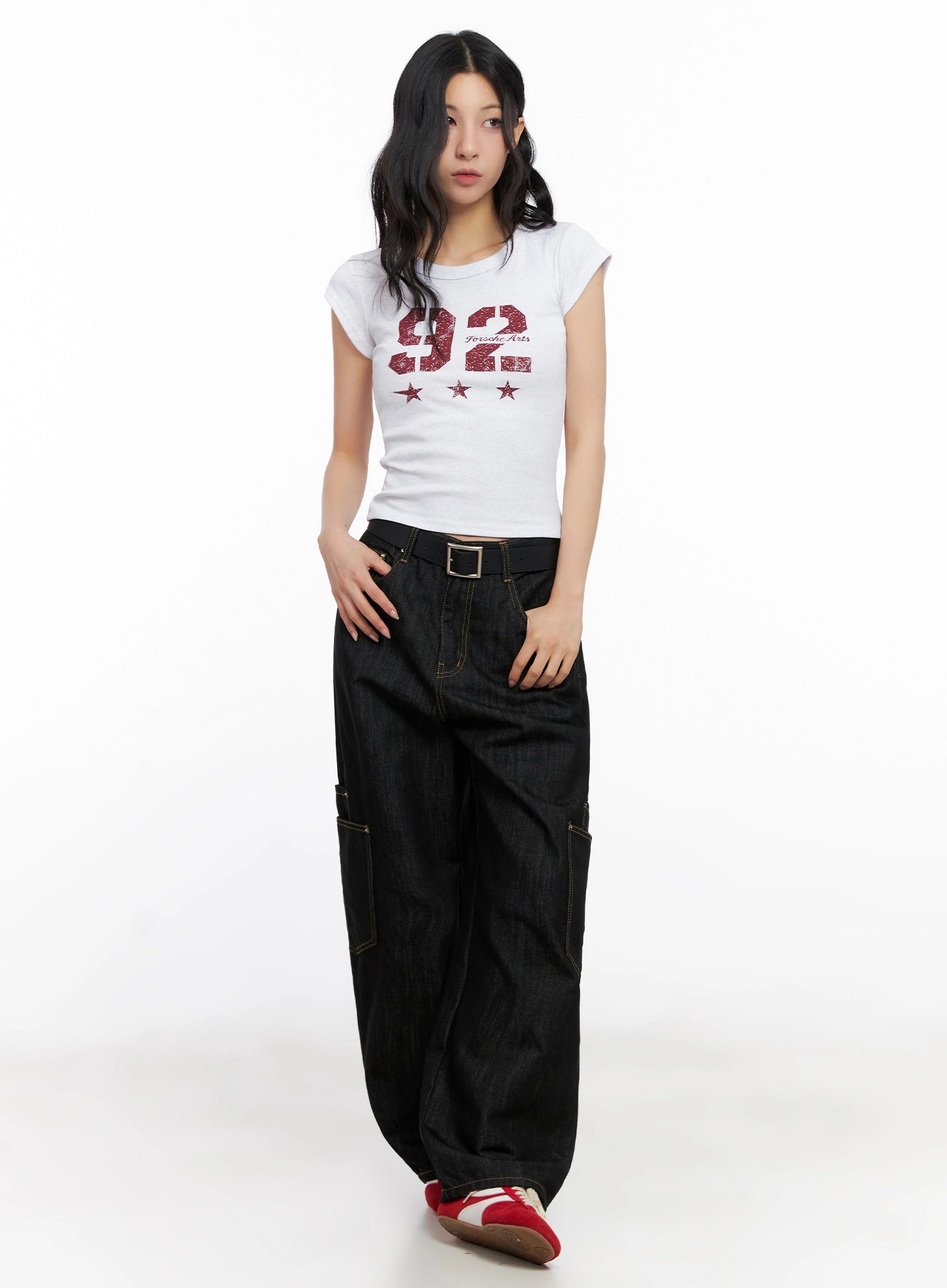 Dahee Wide-Leg Cargo Jeans IG508 in black, full-body front on model, styled with white graphic crop tee and black belt, wide cargo-pocket leg in cotton denim, paired with red and white sneakers.