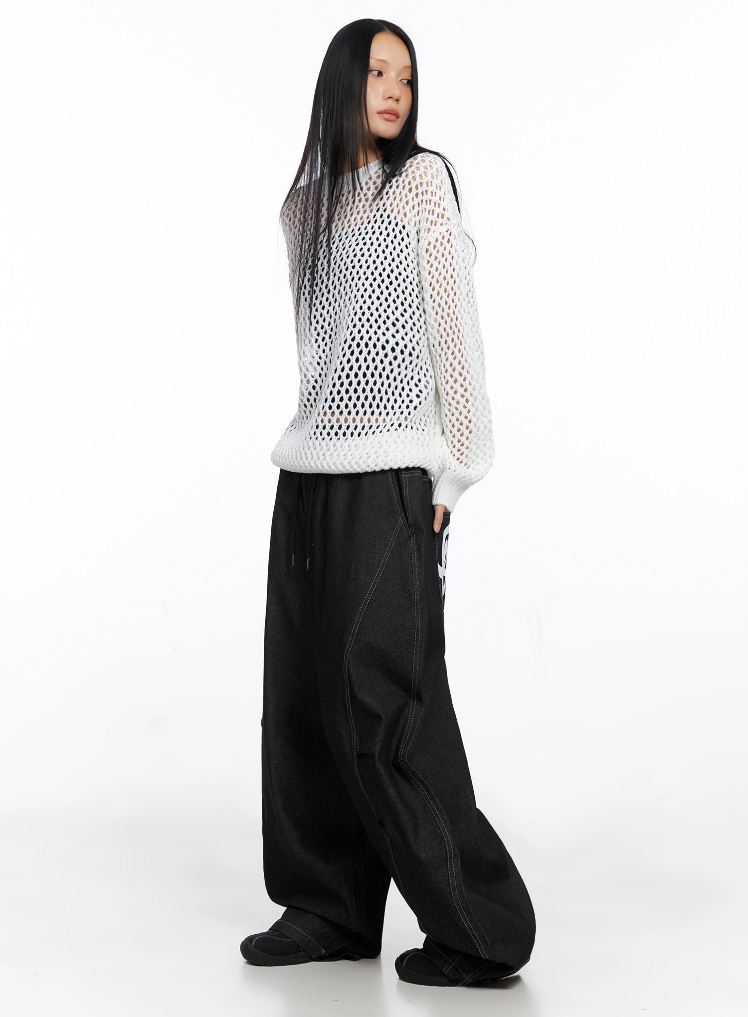 Ayra Graphic Baggy Jeans IO516 in Black, side full-body on model, baggy long cotton denim with cursive lettering glimpsed on back pocket, layered with white mesh knit top.