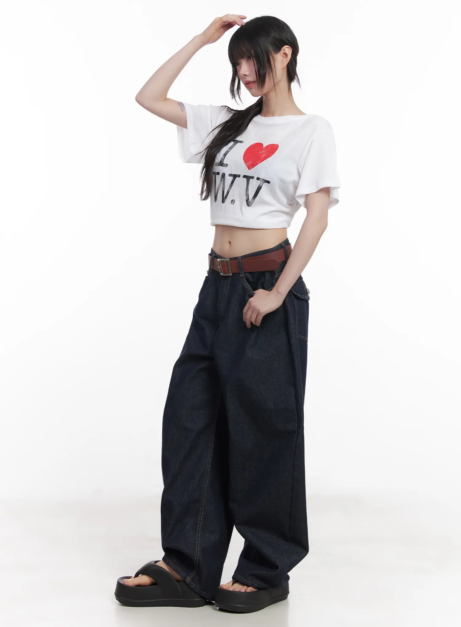 Hyein No-Fade Relaxed-Fit Jeans CU519 in dark blue, three-quarter side view on model, wide-fit silhouette with brown belt, paired with white graphic crop tee and black platform sandals.