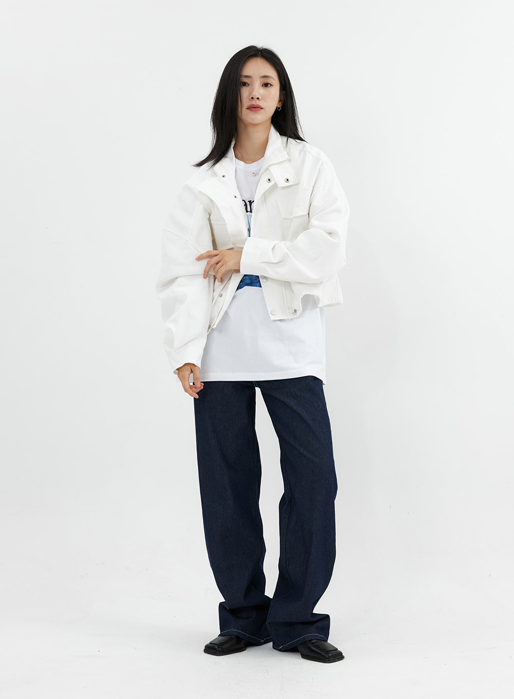 Stitched Jeans OO305 in Blue, front three-quarter view on model arms crossed, wide-fit indigo denim with contrast stitching, styled with white cropped jacket and graphic tee.