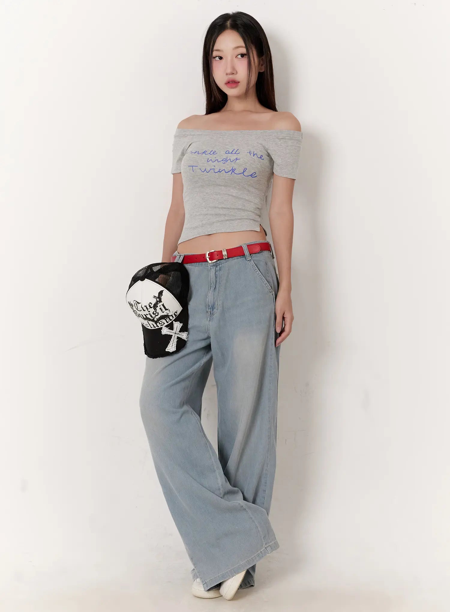 Huening Wide-Leg Jeans CL531 in blue, full-body front editorial shot on model holding cap, washed wide-leg denim with red belt, styled with grey off-shoulder crop top in street look.