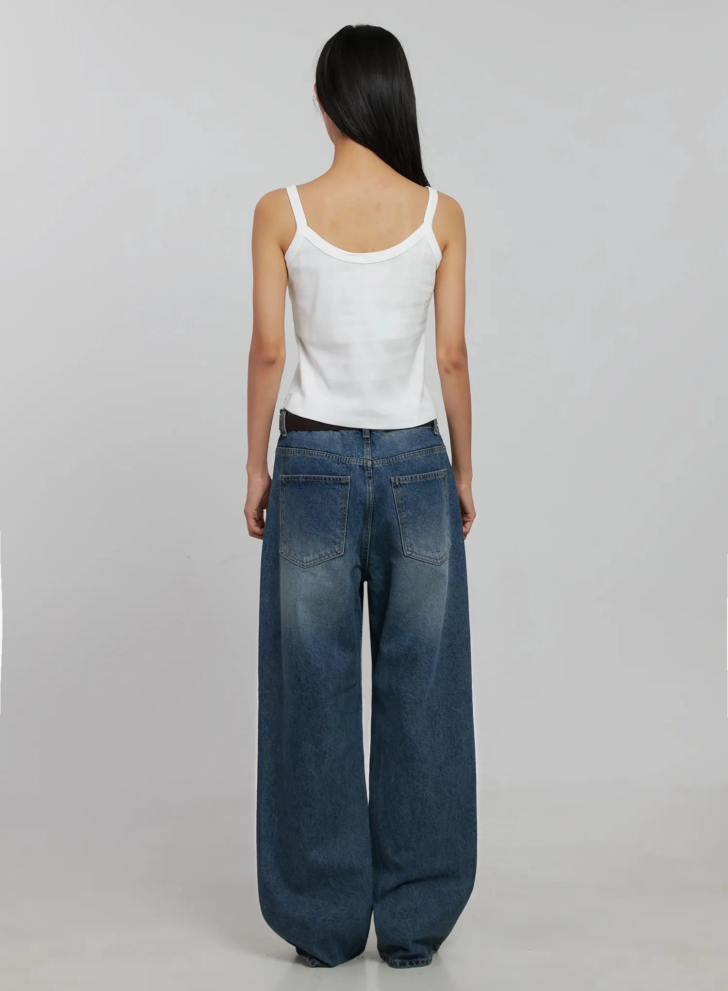 Akira Wide Leg Jeans IJ508 in blue, full back view on model, wide-leg washed cotton with two back patch pockets and brown belt, paired with white cami.