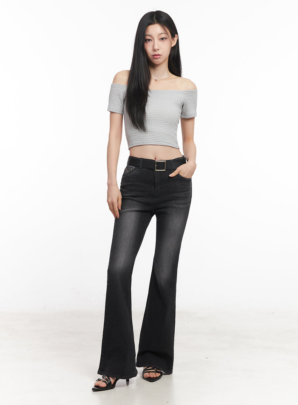 Lior Slim-Fit Bootcut Jeans IY516 in black, full-length front shot on model, darker washed bootcut denim belted at high waist, paired with grey off-shoulder crop top and black strappy heels.