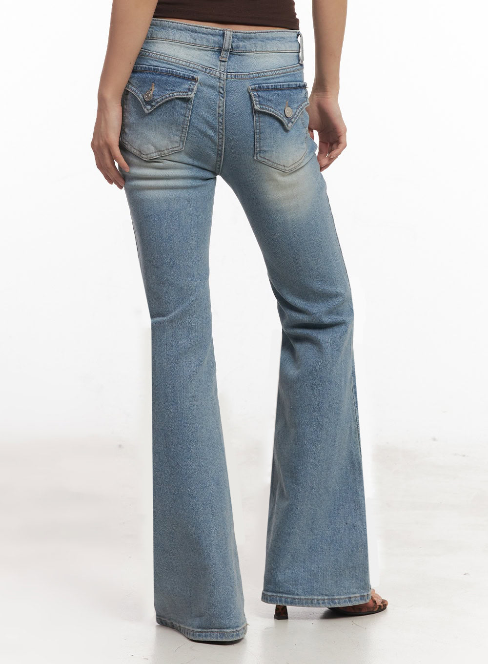 May Washed Flared Jeans IA515 in light blue, back close-up from waist to hem on model, decorative flap back pockets with button detail, heavy washed fading, wide flared leg opening.