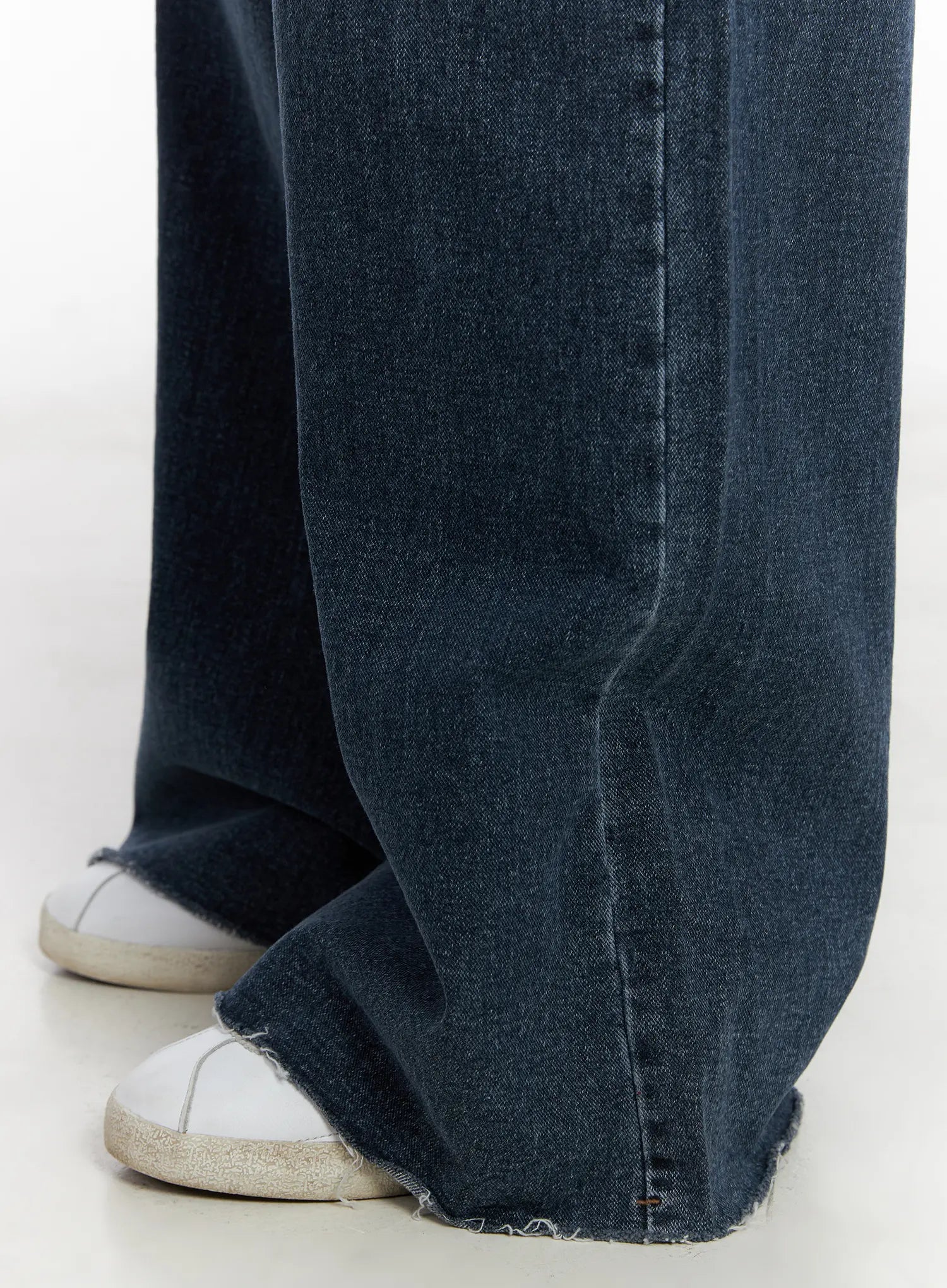 Louisa Ultra Wide Flared Jeans CN527 in dark blue, macro close-up of hem detail, showing raw frayed edge and ultra wide flared leg draping over white sneakers, washed cotton texture visible.