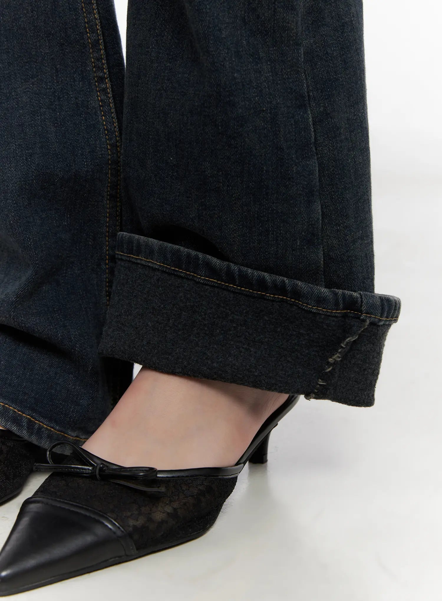 Jay Dark-Wash Bootcut Jeans CD501 in dark blue, macro close-up of bootcut hem on model, raw-edge unfinished hem detail with gold stitching, worn with black kitten-heel mules.