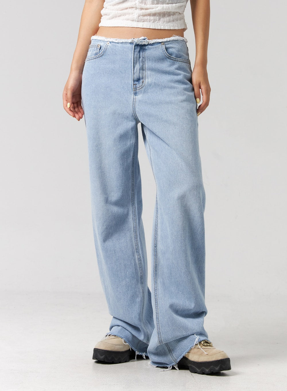 Cut Waist Wide Leg Jeans CG323 in light blue, angled front waist-to-hem shot on model, frayed cut waist and diagonal seam detail visible, wide-leg cotton denim with raw hem.