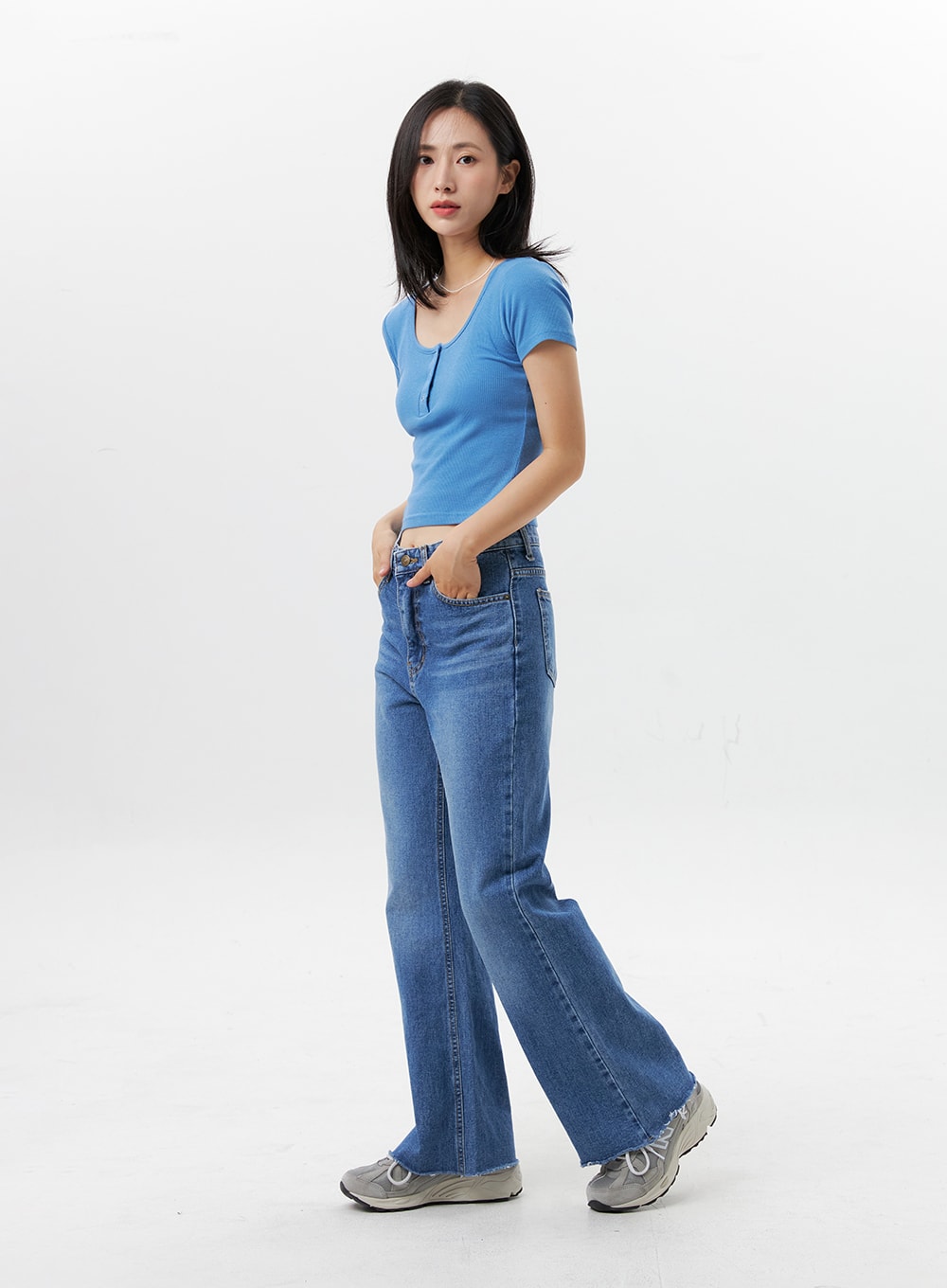 Straight-Leg Jeans OG318 in medium blue, three-quarter side view on model, walking pose showing leg line and raw frayed hem, high-rise fit, styled with blue short-sleeve ribbed crop top.