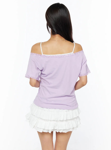 Lace Trim Off-Shoulder Tee CU522 in light purple, back view on model, lace trim across back off-shoulder neckline and sleeve cuffs, clean back silhouette, styled with white tiered ruffle mini skirt.