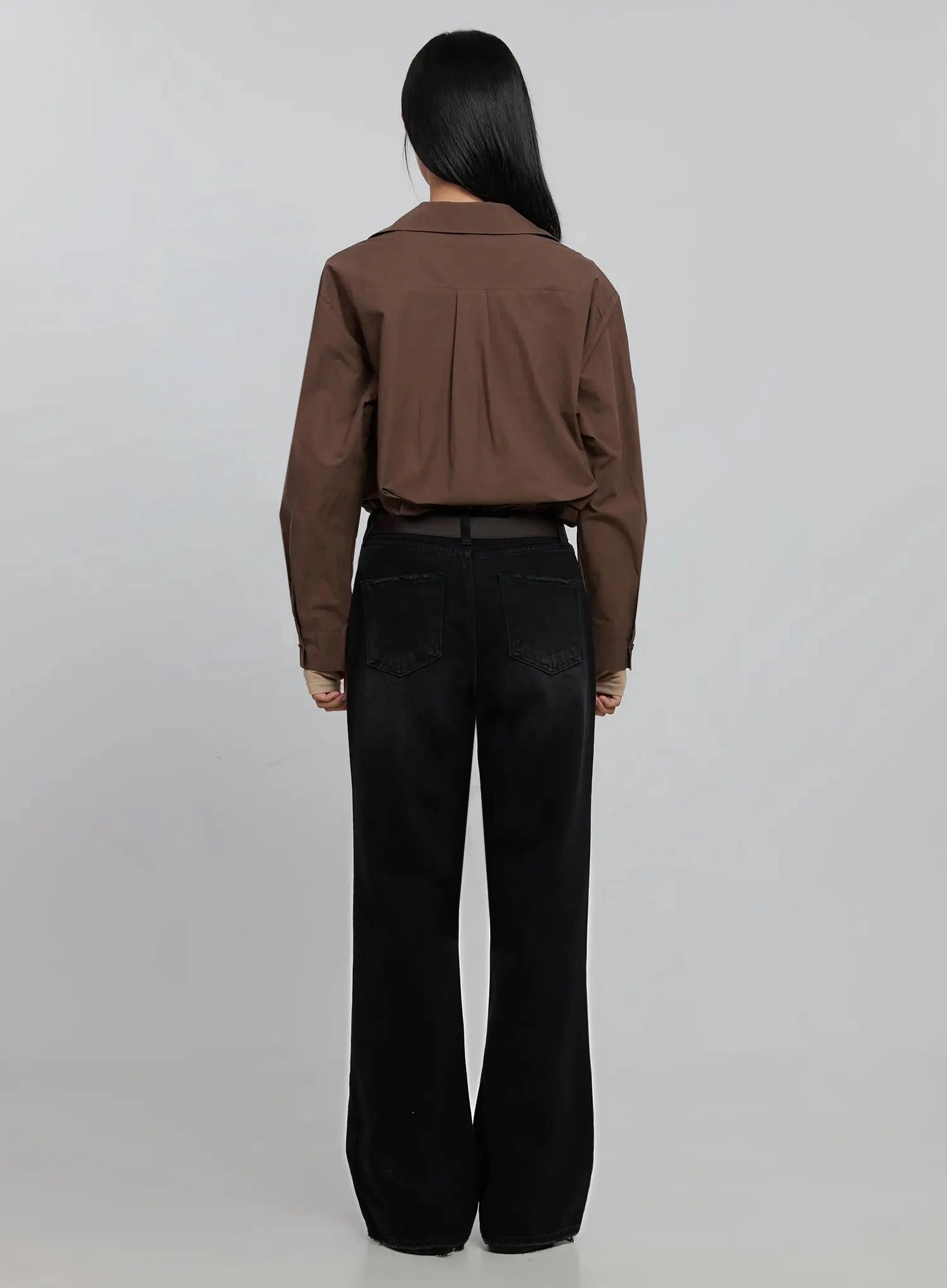 Imani Wide-Leg Flared Jeans ID516 in black, back view on model, showing two back pockets with stitching, flared hem, dark belt at waist, brown shirt on top, full-length cotton denim.
