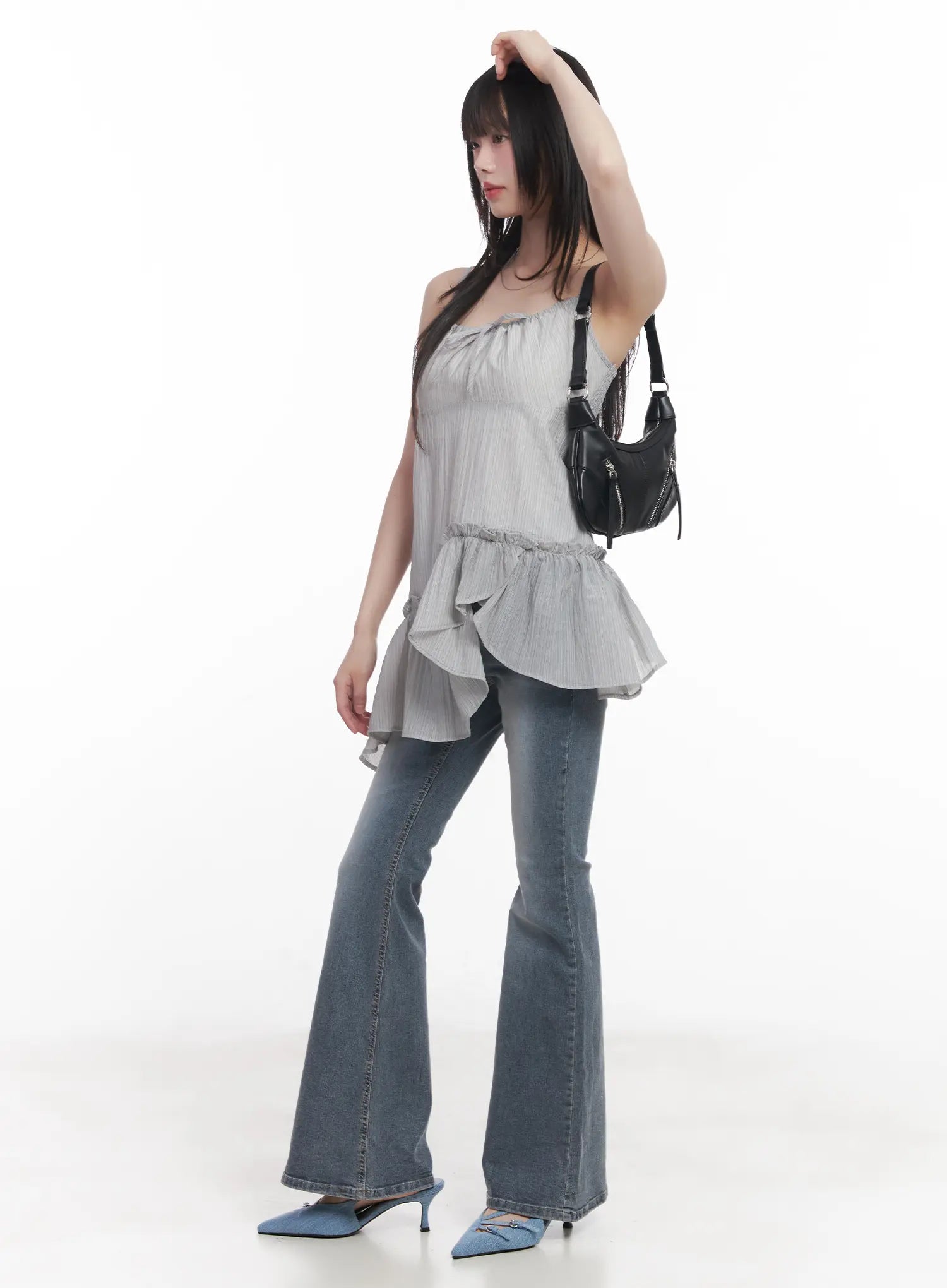 Soyeon Flared Jeans with Hip Pads CU520 in dark gray, front three-quarter on model in dynamic pose, washed flared jeans with ruffle cami and black crescent bag, blue mules.