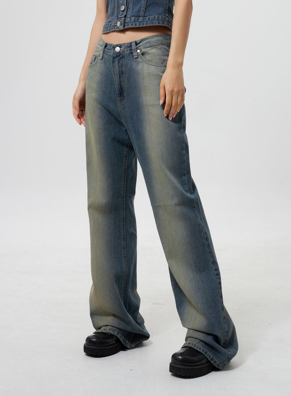 Low Rise Wide Leg Jeans CY323 in vintage blue, front angled mid-shot on model, low-rise wide-leg denim with pronounced yellow-green fade wash, floor-grazing hem pooling over black chunky boots.
