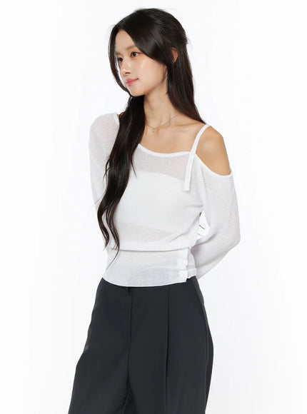 One-Shoulder Knit Top CU522 in white, three-quarter front-side view on model, sheer fine knit with asymmetric cold-shoulder and thin strap, side button hem detail, paired with black trousers.