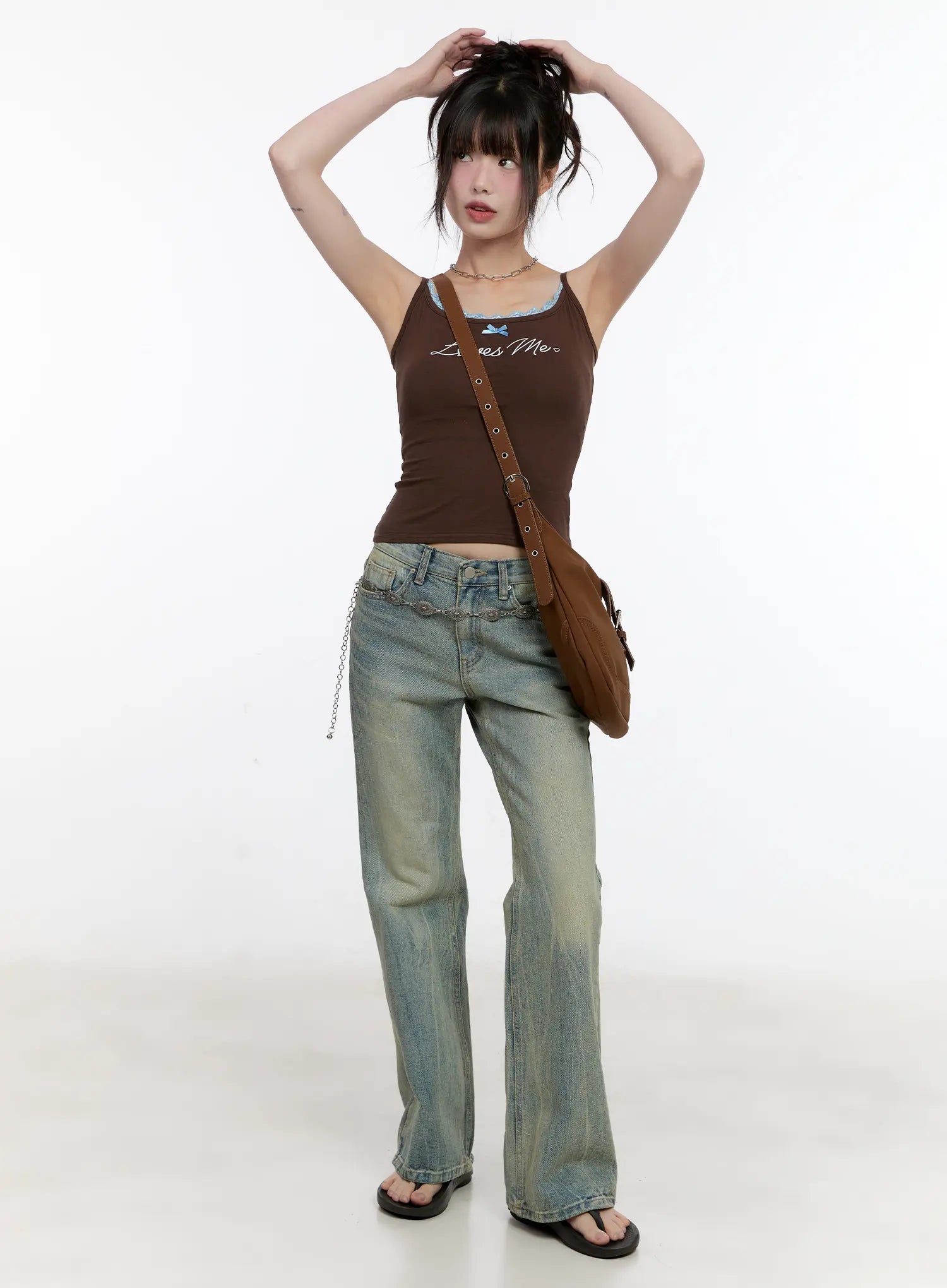 Roa Vintage Blue Flared Denim Jeans CL504 in blue, full-body front shot on model with arms raised, vintage washed flared denim with chain belt, styled with brown graphic cami and crossbody bag.