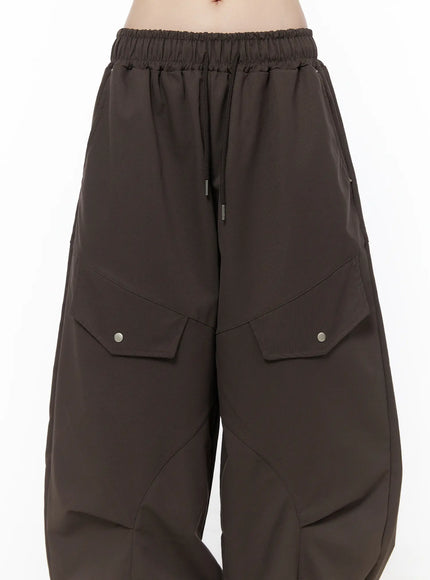 Wide Leg Pintuck Cargo Pants CU519 in dark brown, waist and thigh close-up on model, elastic drawstring waistband and dual snap-button cargo flap pockets with pintuck seam detail.