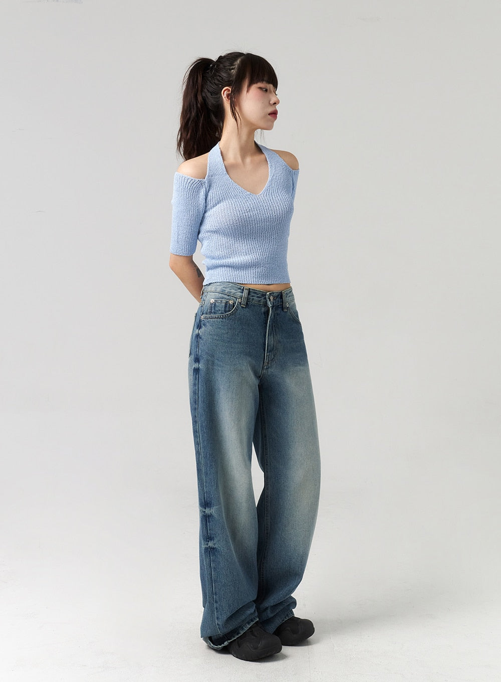 Mid-Wash Baggy Jeans CL312 in mid-wash blue, three-quarter side view on model looking away, wide baggy leg with faded vertical streaks, hem trailing over black chunky shoes.