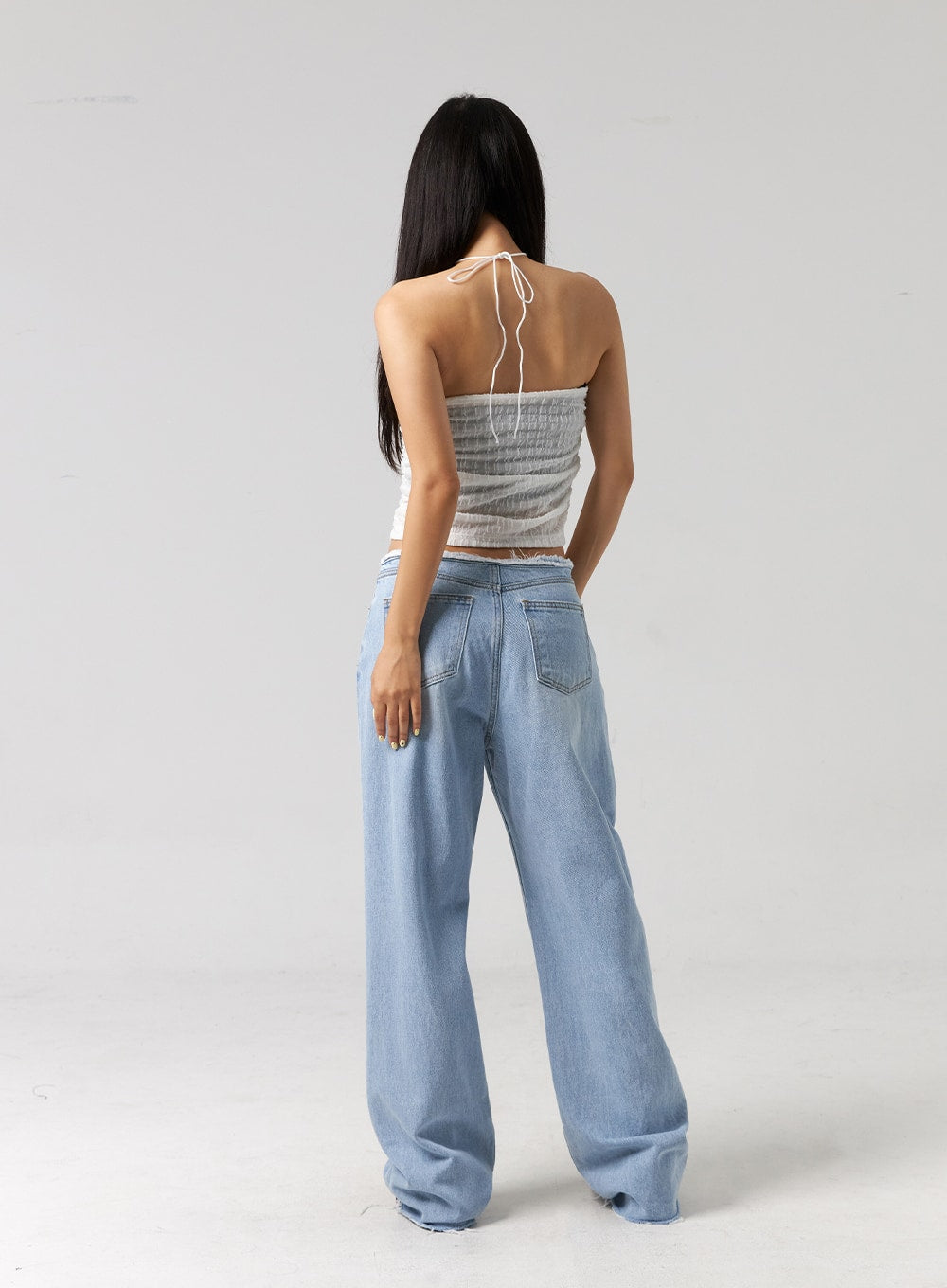 Cut Waist Wide Leg Jeans CG323 in light blue, full-body back shot on model, wide relaxed leg with back pockets, frayed cut waistband, raw-hem ankle, paired with white halter top.