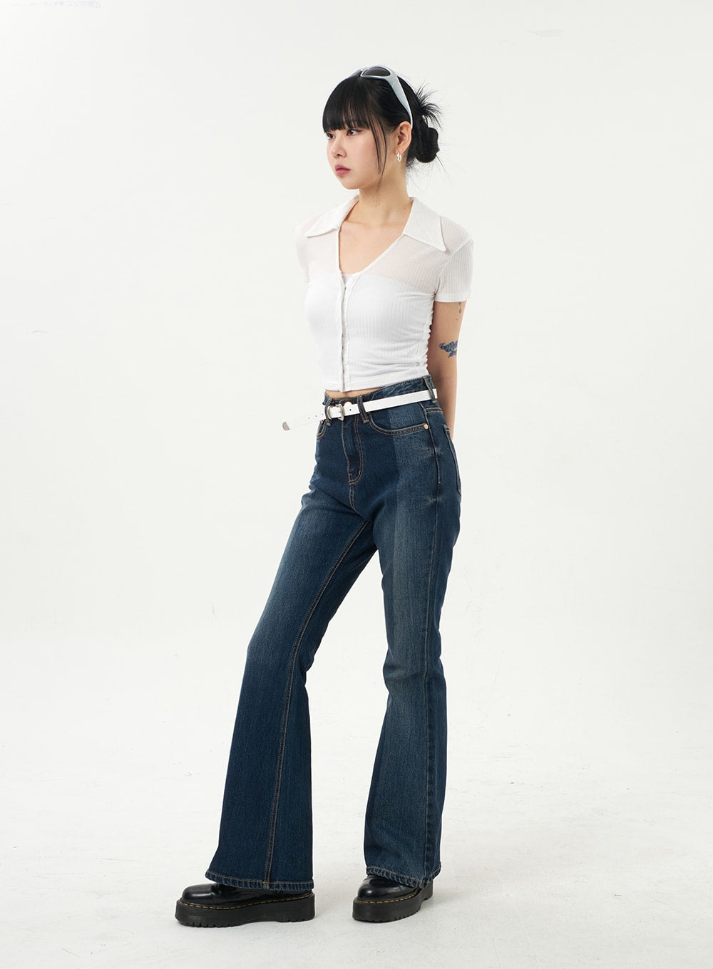 Dark Wash Bootcut Jeans CA328 in dark blue, front 3/4 view on model looking away, slim-fit washed denim, high waist with white belt, full bootcut length over black boots.