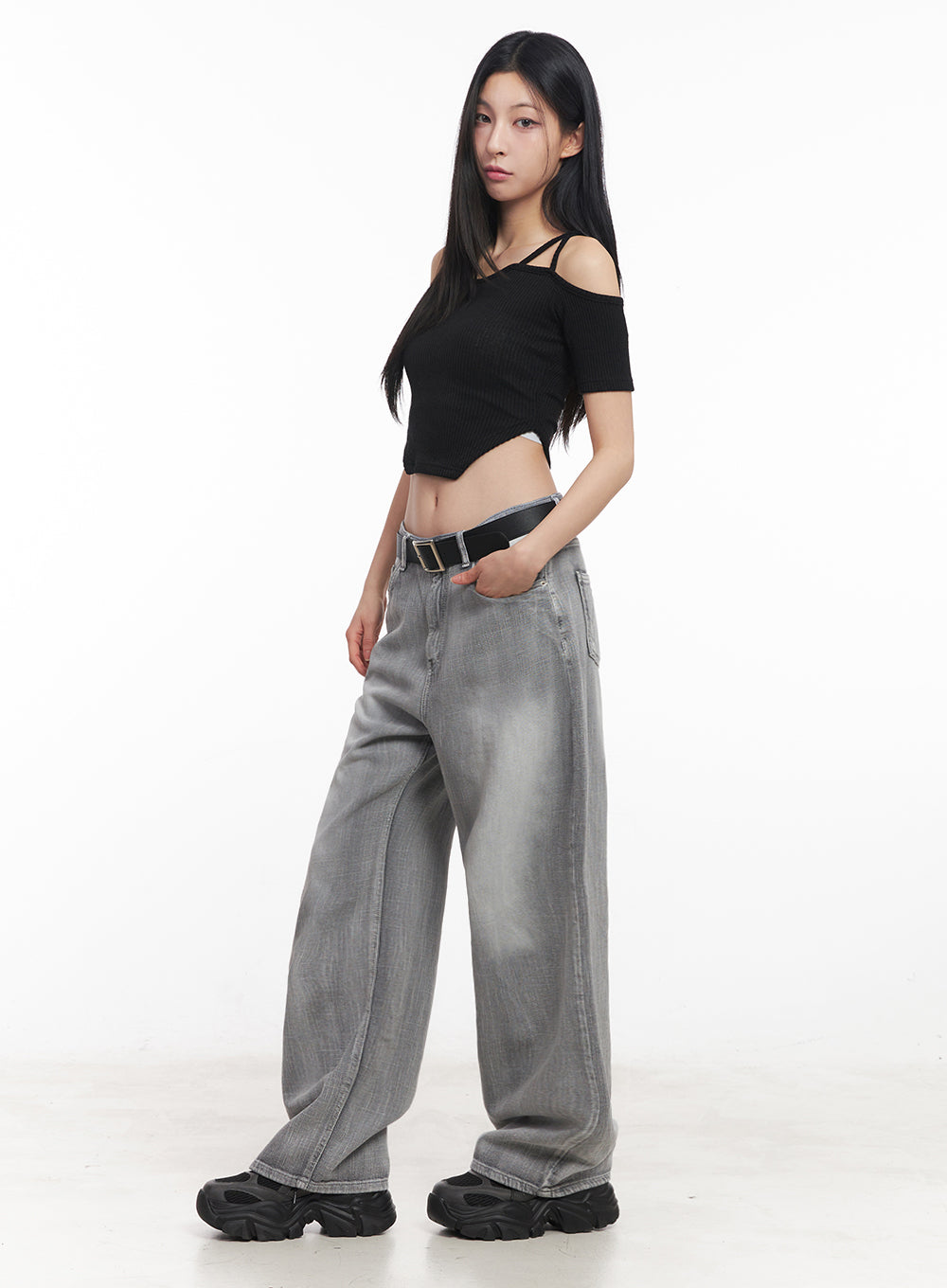 Flore Washed Wide-Leg Jeans IY516 in gray, side view on model, low-rise wide-leg washed denim with black belt, styled with black cold-shoulder crop top and chunky sneakers.