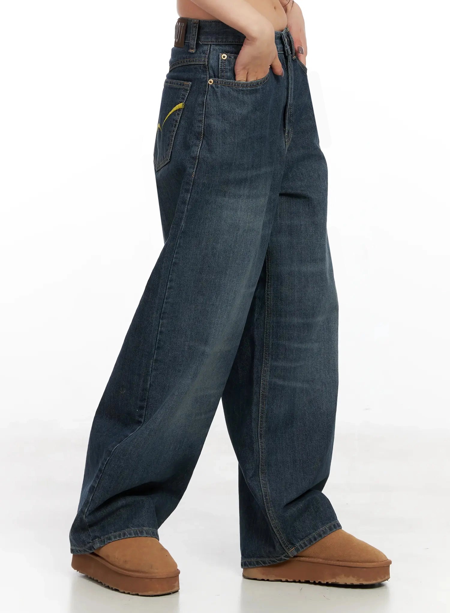 Regina Contrast Stitch Baggy Jeans IN528 in dark blue wash, side close-up on model, yellow contrast stitch embroidery on side pocket visible, wide-fit washed denim with brown belt and tan boots.