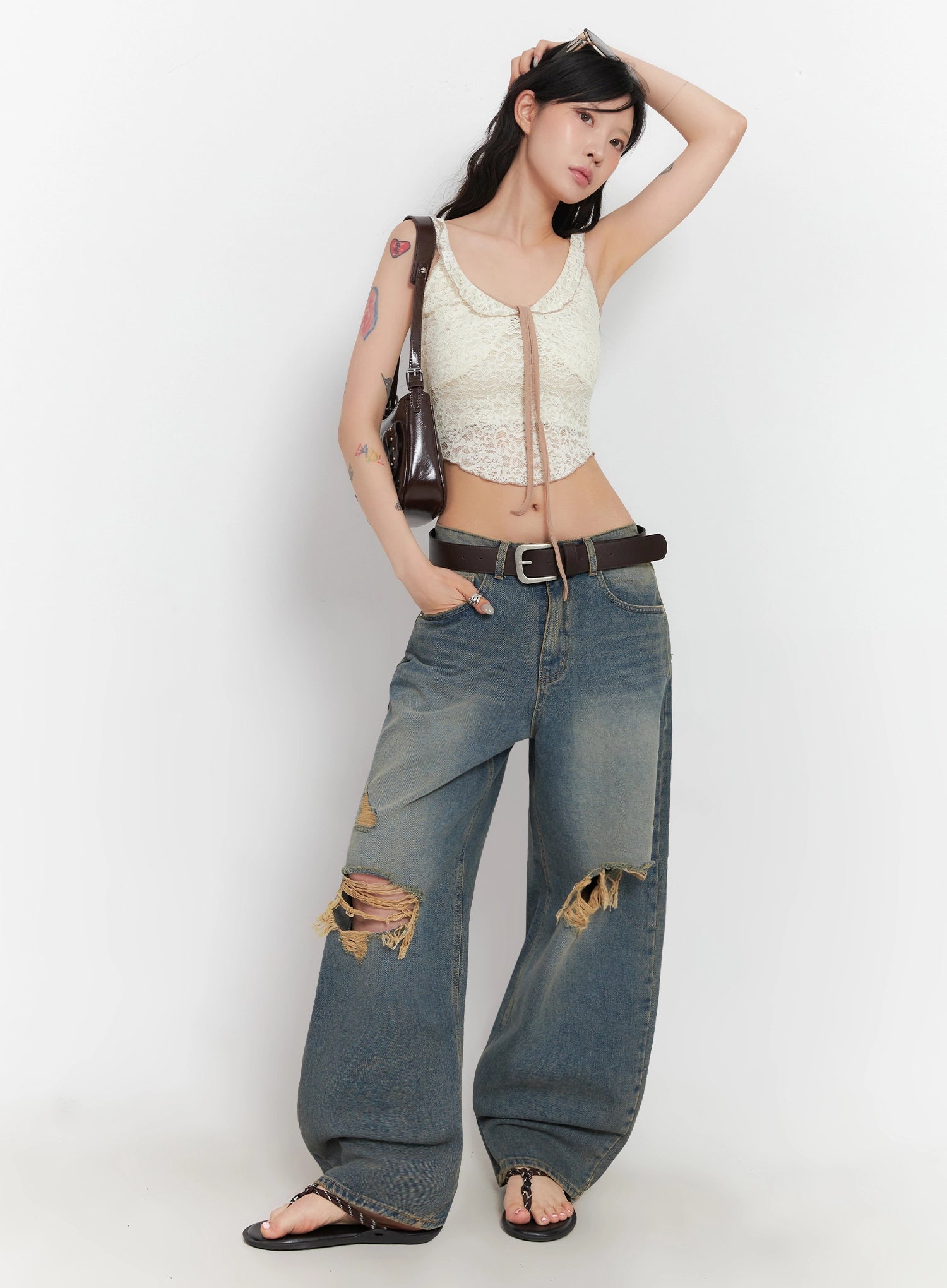 Jeemin Vintage Distressed Wide-Leg Denim Jeans IC503 in washed blue, three-quarter front view on model, candid pose with hand in hair, styled with lace crop top, belt, and brown shoulder bag.