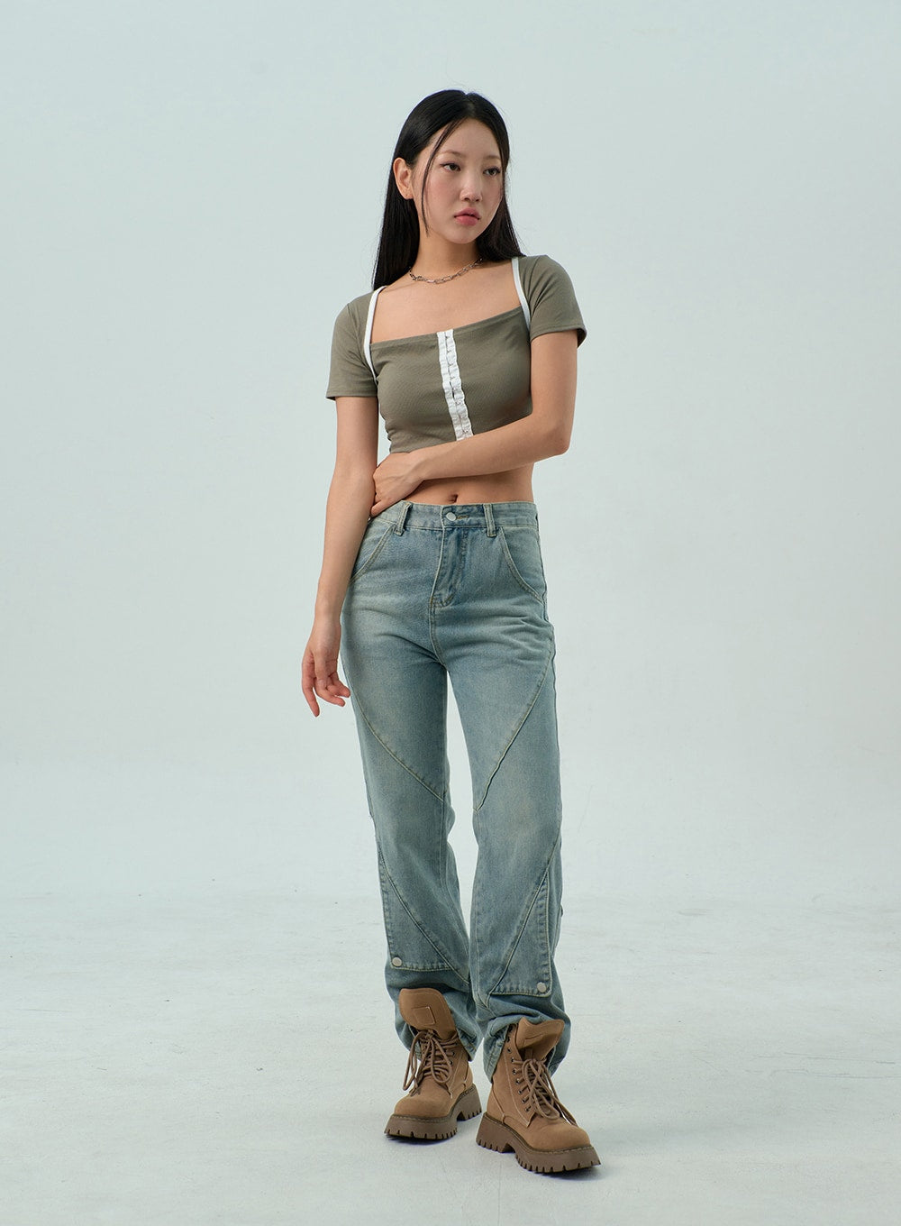 Straight Leg Jeans CY330 in light blue wash, full-length three-quarter front shot on model, arm across waist pose, geometric panel seams and snap-button hem detail visible, tan lug boots.