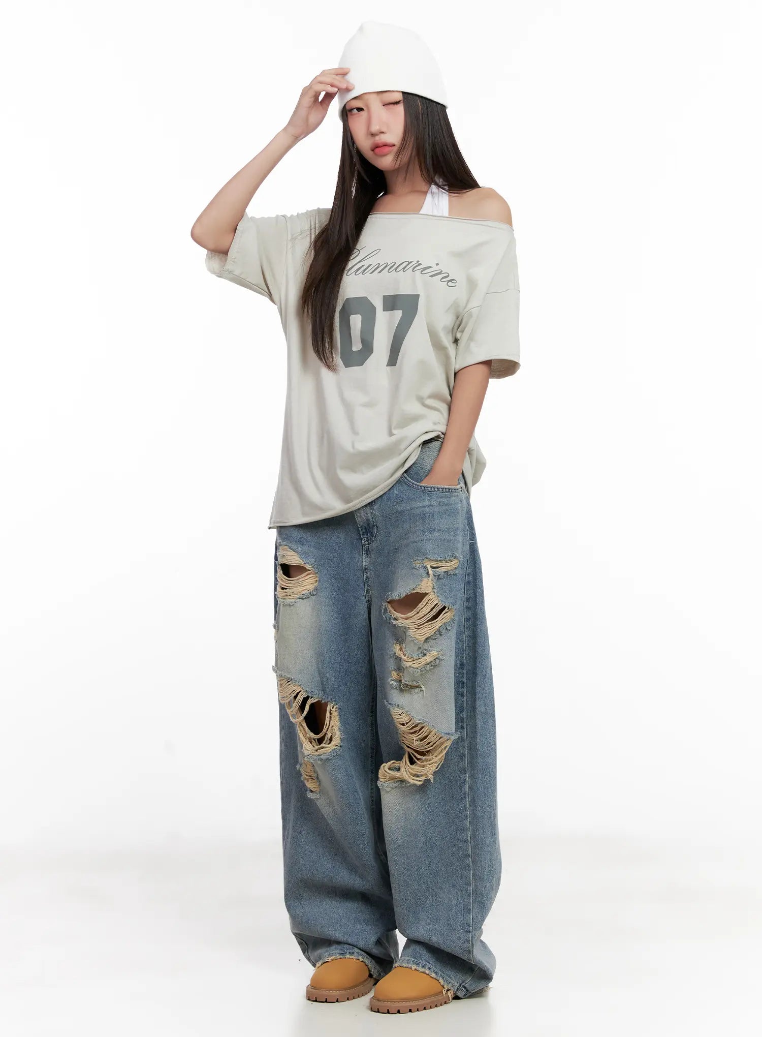 Manon Washed Distressed Wide Jeans CL518 in blue, full-body front pose with hand on beanie, heavy destroyed detailing on thighs, paired with off-shoulder graphic tee and chunky boots.