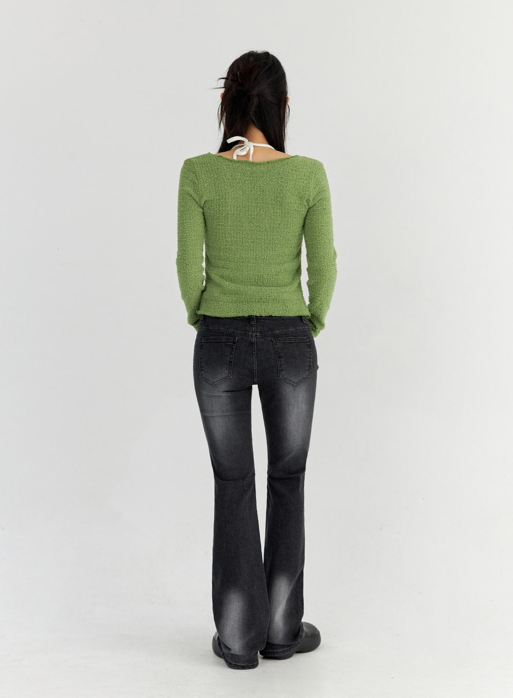 Bootcut Washed Jeans CO325 in dark gray, back full-body view on model, back patch pockets with chevron stitching, slim bootcut silhouette, washed denim, paired with green knit top.