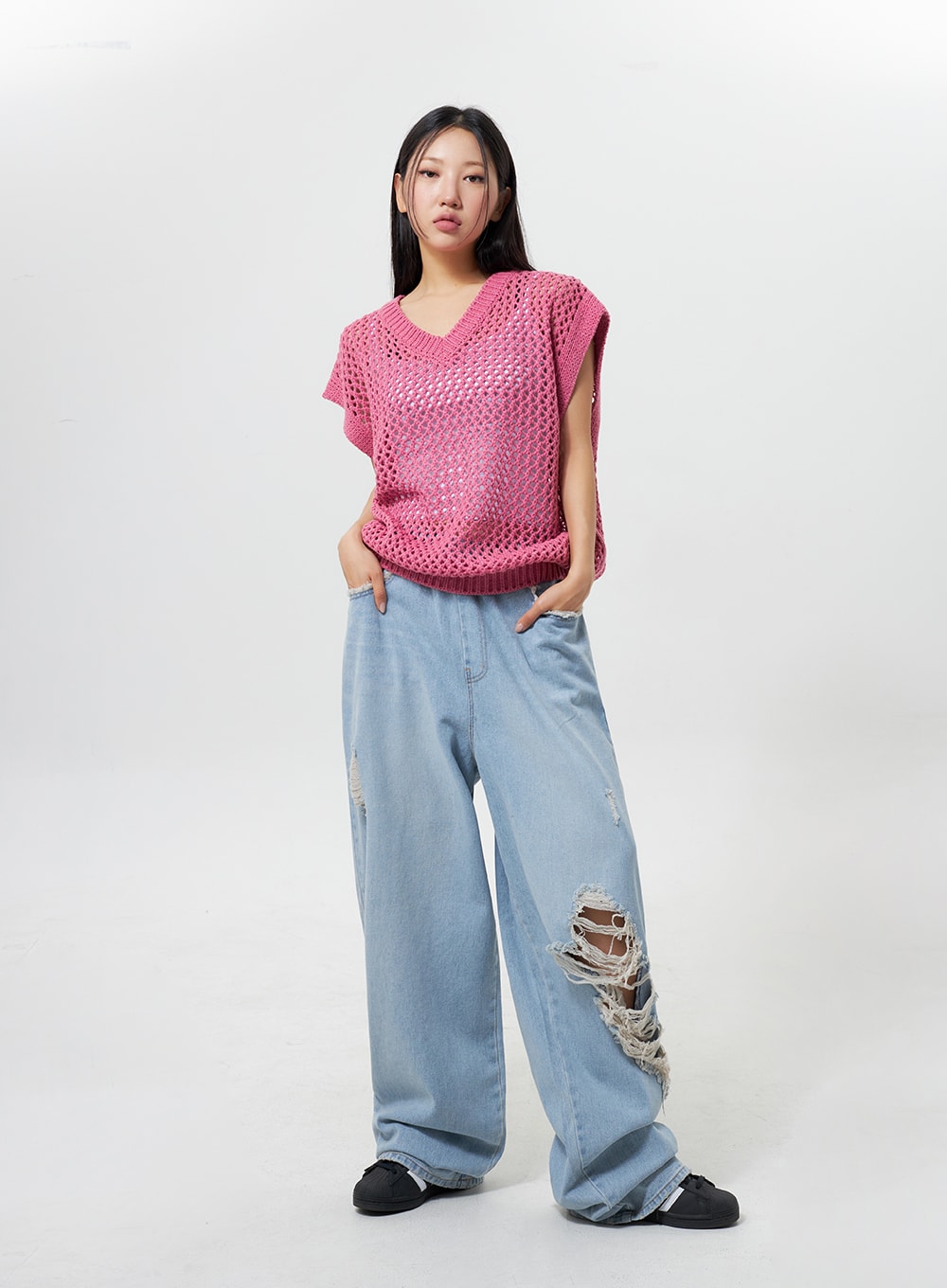 Oversized Ripped Jeans CY324 in light blue, full-body slight angle on model, wide-leg light-wash denim with ripped distressing, hands in pockets, paired with pink crochet vest.