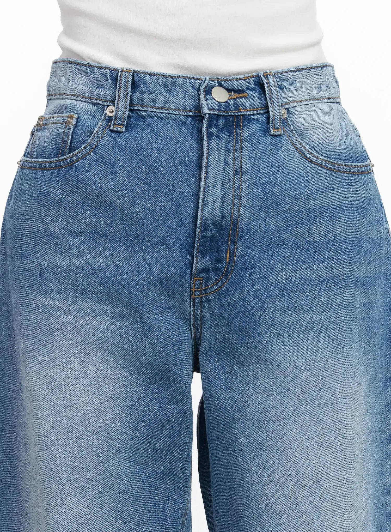 Iliana Wide Leg Jeans IJ529 in blue, front waistband detail close-up on model, showing metal button, five-pocket construction and washed denim fade at thighs.